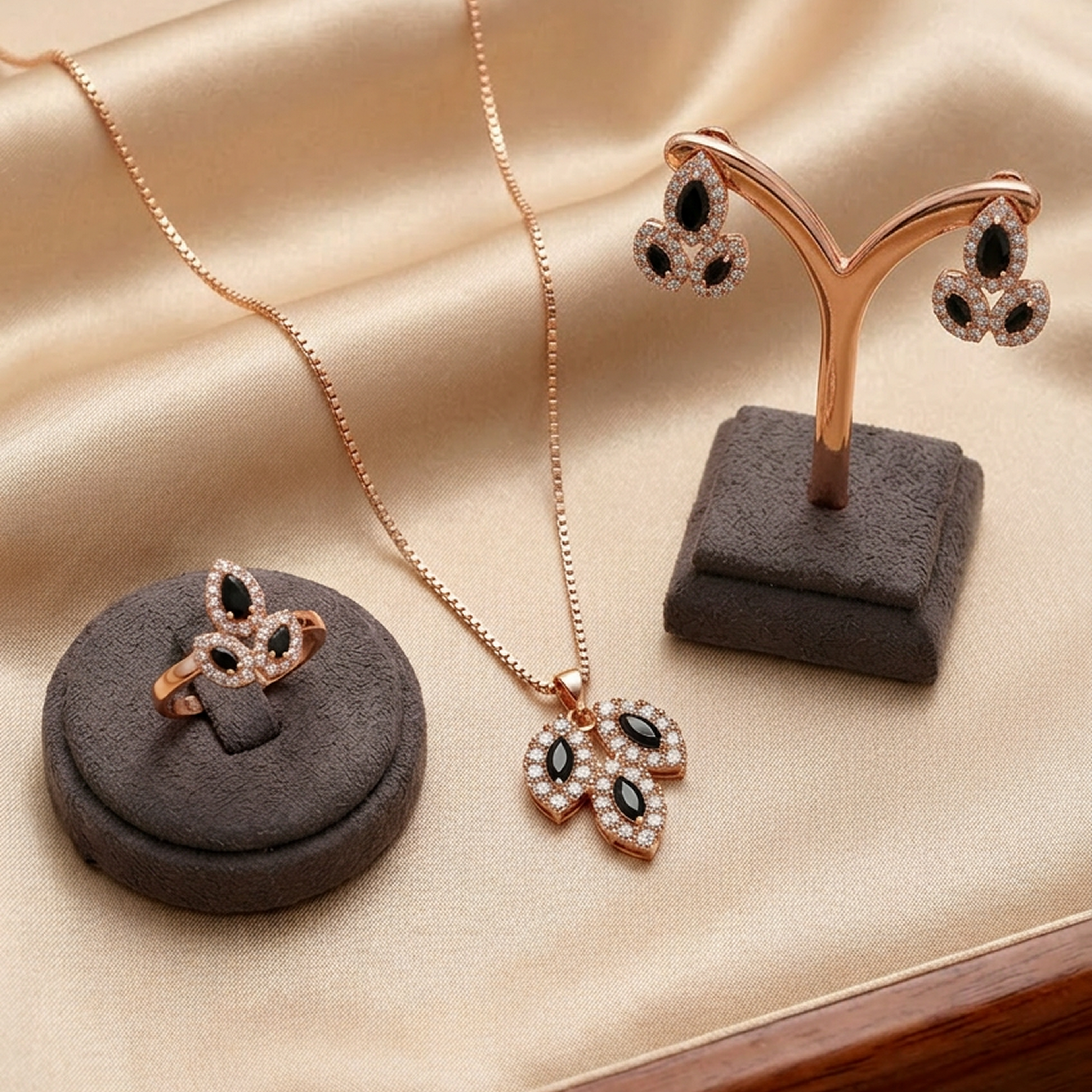 Rose gold-toned leaf stone jewelry set by Zaraya Store, featuring a necklace, ring, and earrings with black and clear gems on a beige fabric.