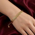 A gold-toned and pavé crystal stack bracelet by Zaraya Store worn on a wrist against draped maroon fabric.