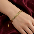 A gold-toned and pavé crystal stack bracelet by Zaraya Store worn on a wrist against draped maroon fabric.