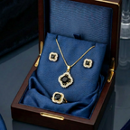 Black stone and gold jewelry set in a decorative quatrefoil shape, presented in an open blue velvet-lined wooden box.