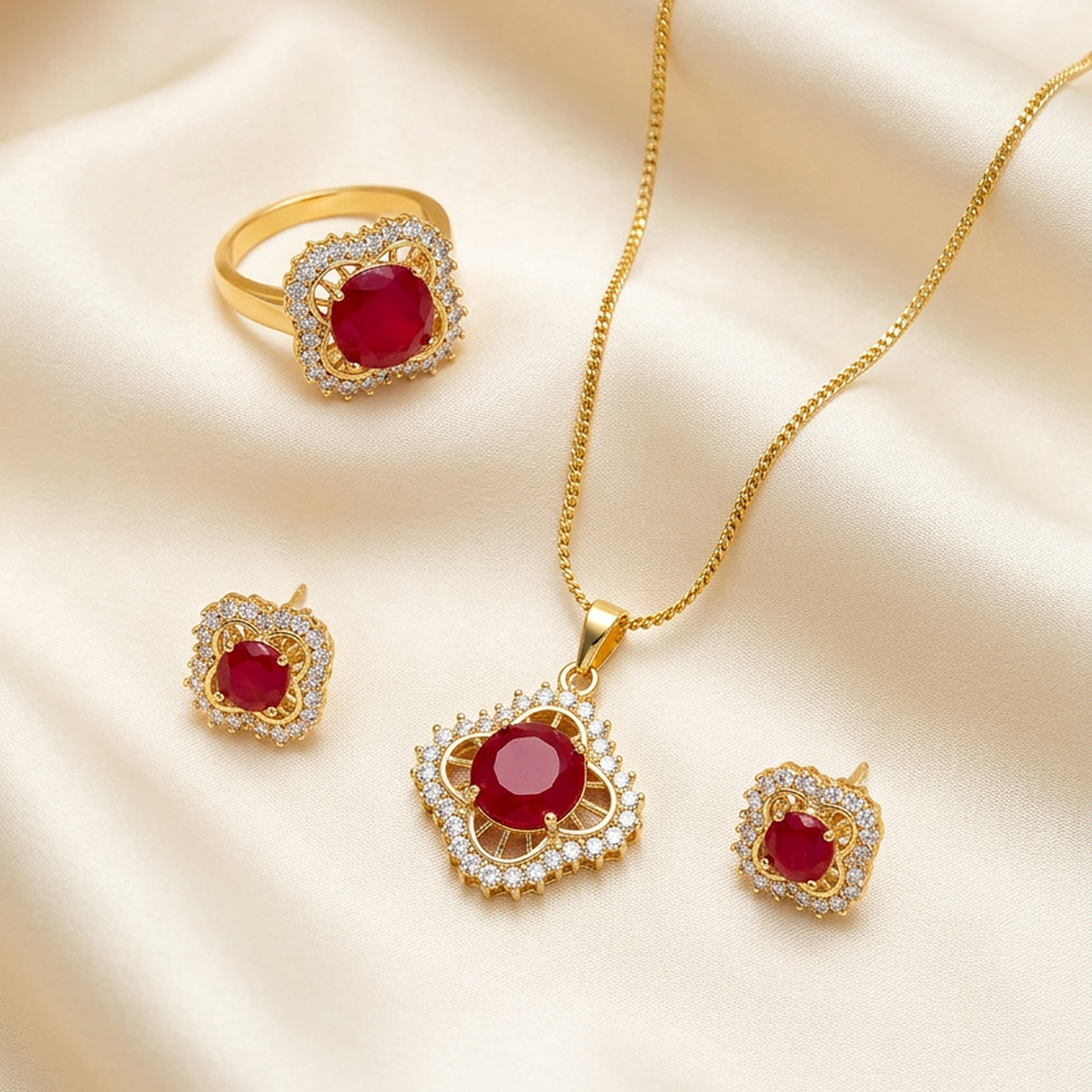 Gold jewelry set with red round stones and clear accent stones, including a necklace, ring, and earrings, on cream satin.