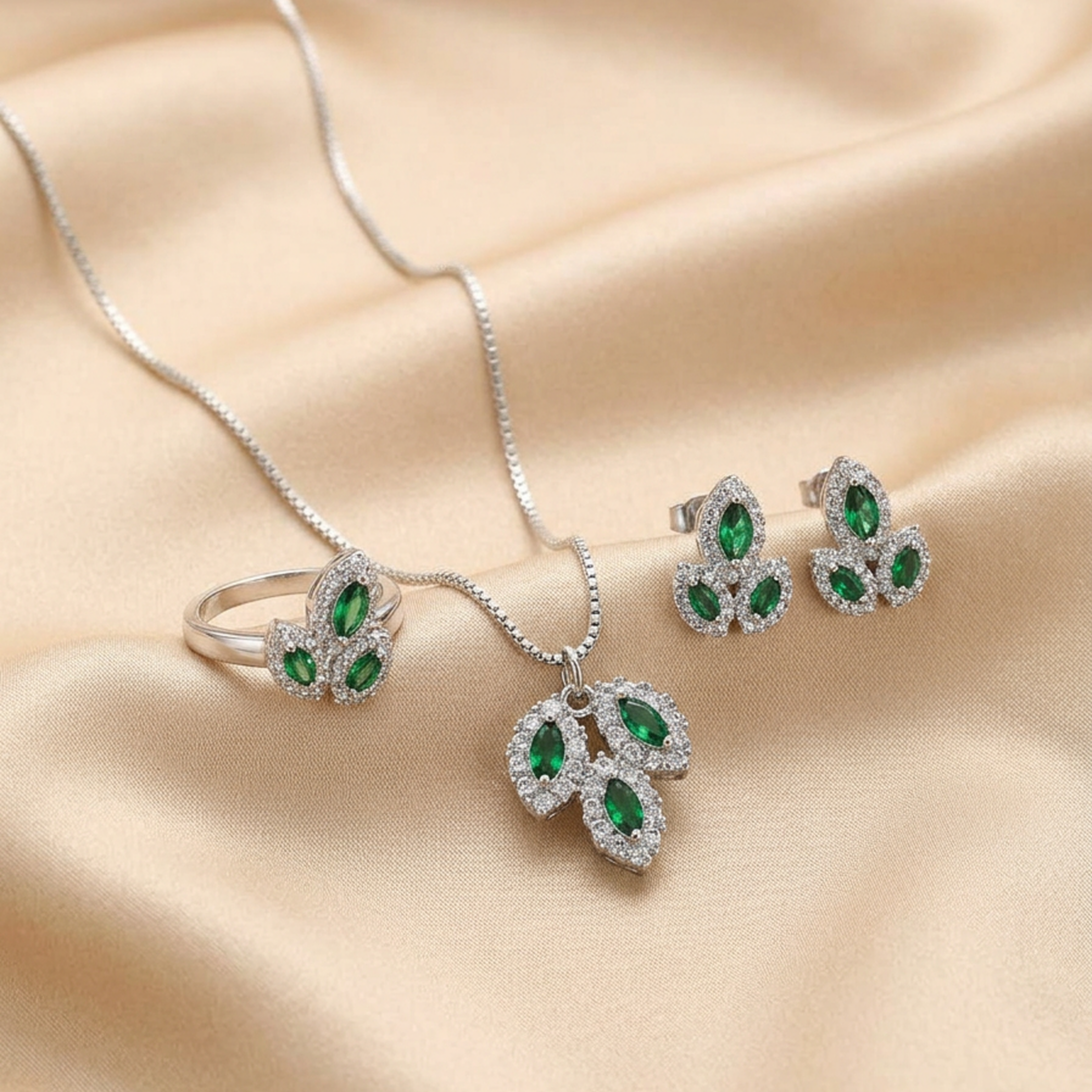 Silver leaf stone jewelry set from Zaraya Store, with emerald green stones in a necklace, ring, and earrings, on beige satin.