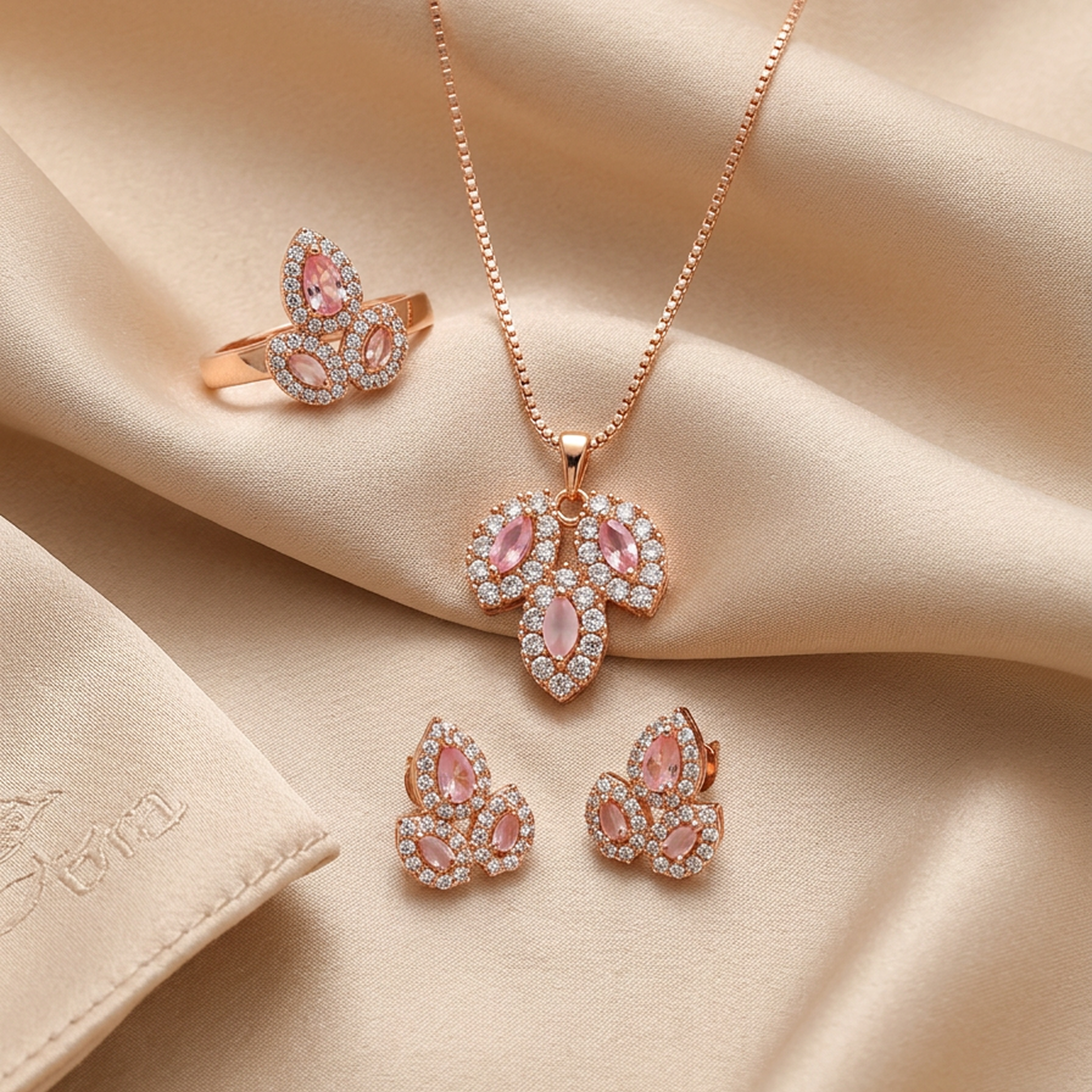 Rose gold leaf stone jewelry set by Zaraya Store, featuring a necklace, ring, and earrings with pink and clear stones, on champagne satin.