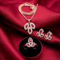 Gold-toned leaf-motif jewelry set with red and clear stones by Zaraya Store, including a pendant, earrings, and ring on red fabric.