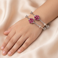 Set of two silver stainless steel bracelets with ruby red floral designs by Zaraya Store, worn on a child's hand against a cream fabric.