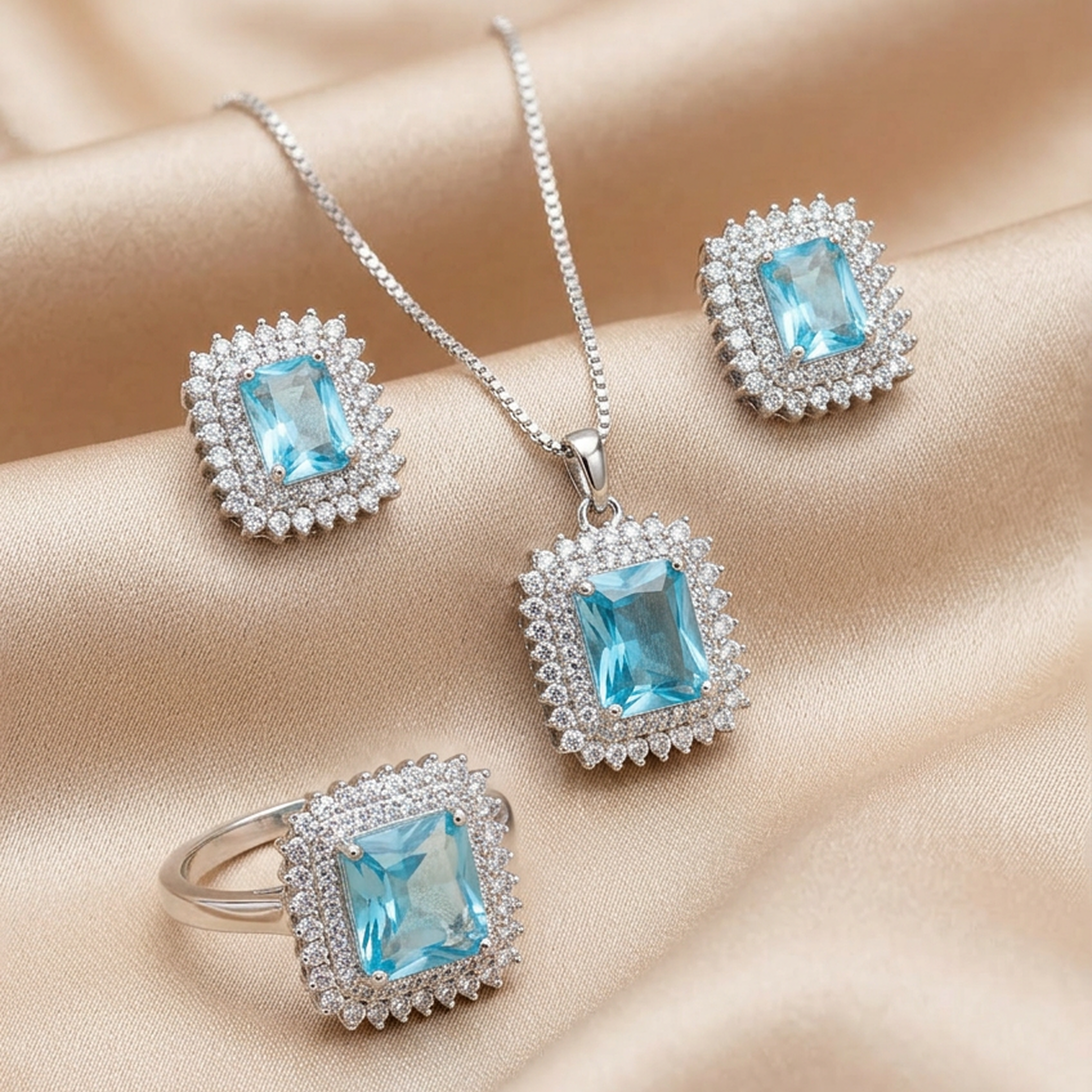Silver jewelry set with blue square stones from Zaraya Store, including necklace, earrings, and ring, each surrounded by small white stones, on beige satin.