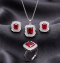 Silver jewelry set with square red and white sparkling stones from Zaraya Store, featuring a necklace, earrings, and ring on dark fabric.