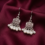 Antique white pearl jhumki earrings by Zaraya Store, with ornate silver-toned metal and hanging pearl drops on maroon fabric.