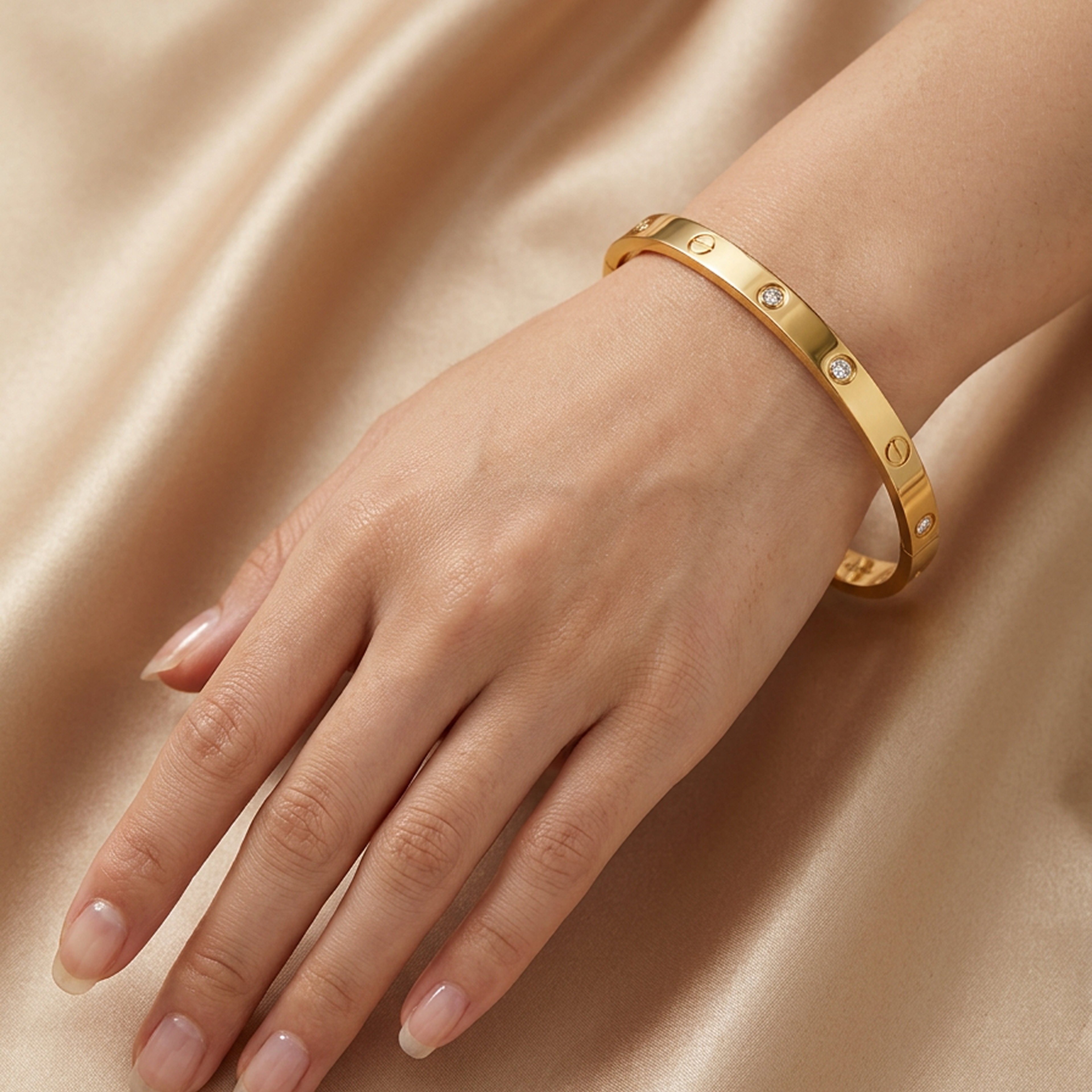 Gold stainless steel iconic screw design bracelet with crystal detail by Zaraya Store, worn on a hand against a champagne silk background.