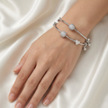 Silver stainless steel adjustable bracelets, a set of two, from Zaraya Store, with crystal orbs, a heart, and bells, on a hand against white satin.