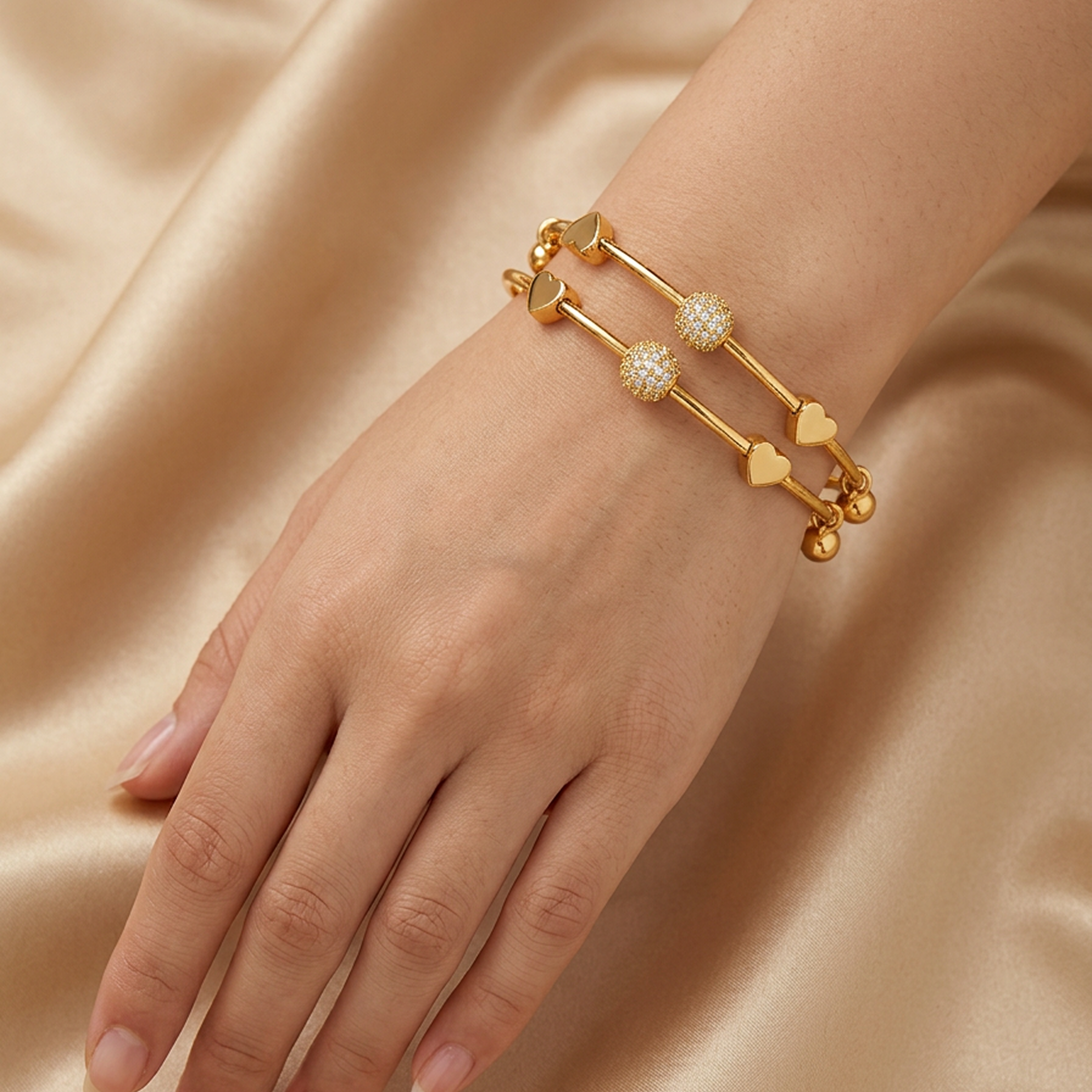 Two gold stainless steel adjustable bracelets by Zaraya Store, featuring crystal orbs and heart charms, worn on a hand against a golden satin background.
