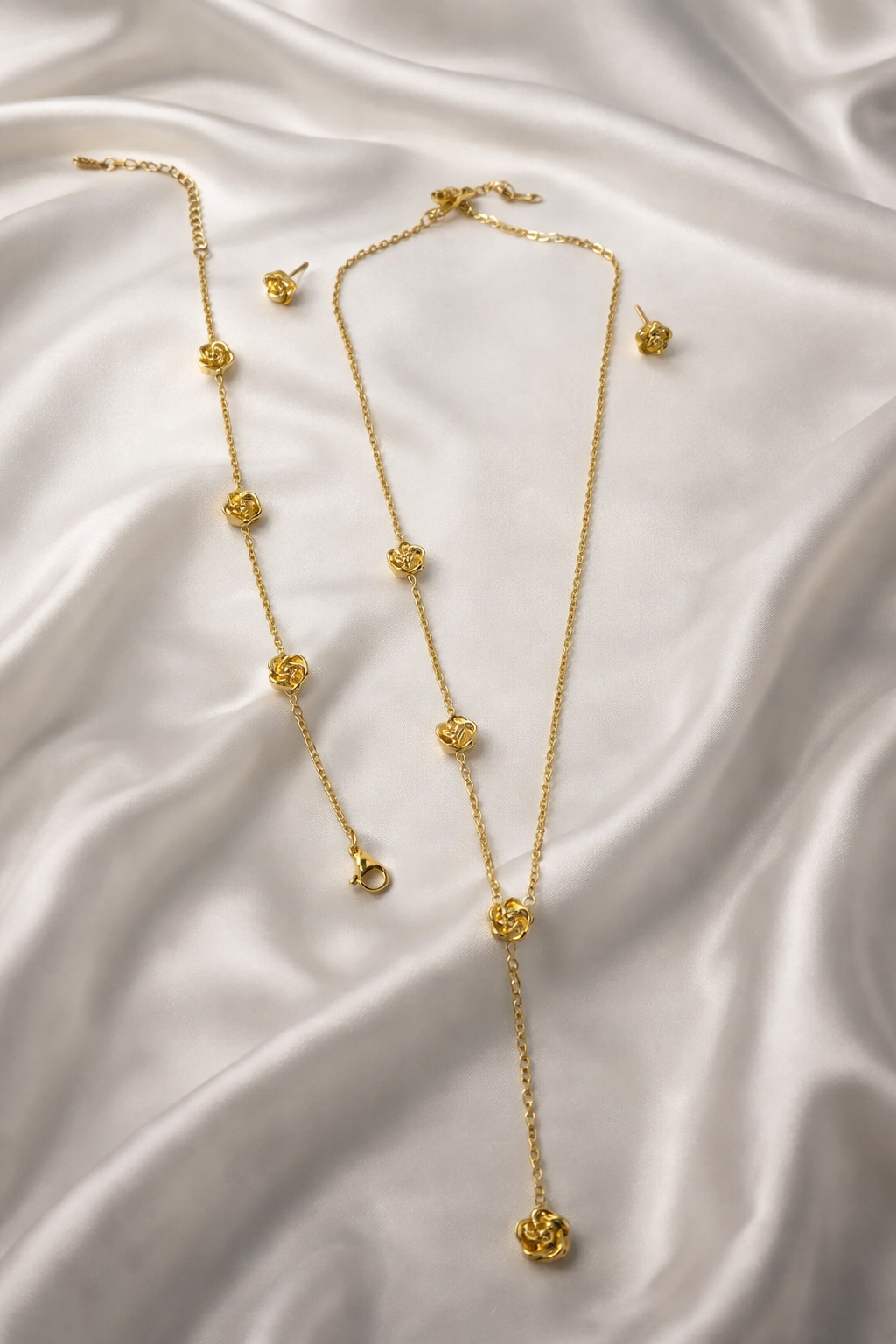 3-piece gold stainless steel rose floral jewelry set with necklace, bracelet, and stud earrings on white satin.